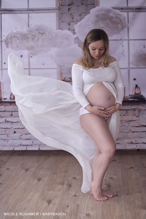Schwangere Frau im weißen Kleid und fliegenden Stoffbahnen