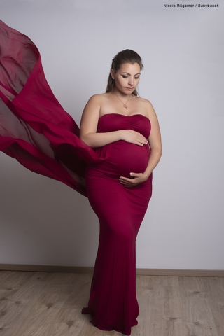 Schwangere im roten Kleid mit fliegenden Stoffbahnen